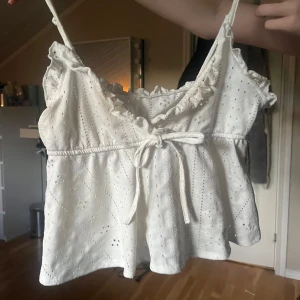 Vit broderad linnetopp med volang och knyt - Superfin vit linnetopp med broderade detaljer, volang vid axelbanden och söt knytning framtill. Perfekt för sommardagar och har tunna axelband. Luftig och lätt i materialet. Stl XS-S