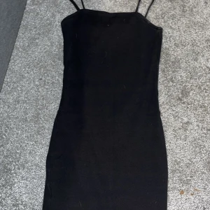 Svart ribbad klänning från Amisu - Säljer en svart ribbad klänning från Amisu med smala axelband och tight passform. Perfekt för dig som gillar en enkel och stilren look. Klänningen är i storlek 32 (XS) och har en klassisk, rak siluett.