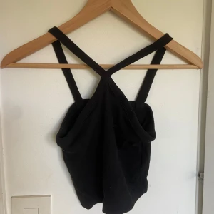 Svart croppad linnetopp från Gina Tricot - Säljer en svart croppad linnetopp från Gina Tricot med smala axelband som korsas i ryggen. Toppen är ribbad och har en enkel, stilren design som passar perfekt till sommaren.