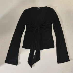 Svart långärmad topp med knyt från Gina Tricot - Säljer en svart långärmad topp från Gina Tricot i storlek XXS. Toppen har snygg knytdetalj framtill och är perfekt att styla med jeans eller kjol för en fin outfit. Använd 3 gånger och är i mycket bra skick! Nypris 299😽❤️