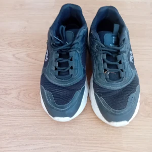 Svarta sneakers från Fila - Säljer ett par svarta Fila sneakers med vit sula och snörning. Skorna har en sportig design med meshdetaljer och Fila-logga på sidan. Perfekta för dig som gillar en klassisk och stilren look.
