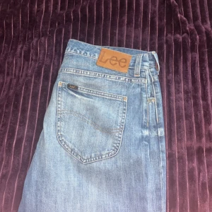 Blå Lee jeans med raka ben - Säljer ett par klassiska blå jeans från Lee med raka ben och normal passform. Jeansen har fem fickor, Lee-logga på bakfickan och knappstängning framtill. Perfekta till vardags för en avslappnad stil.