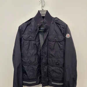 Mörkblå vindjacka från Moncler storlek xxs/0 - En snygg mörkblå Moncler windbreaker med dragkedja och knappar i storlek 0. Den är i super bra skick och är perfekt för lite varmare och blåsiga dagar inför sommaren.