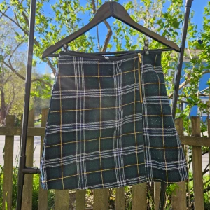 Grön rutig kjol med dragkedja - Snygg grön kortkjol med rutigt mönster i vitt och gult. Kjolen har en guldfärgad dragkedja framtill som detalj. Perfekt för dig som vill ha en trendig och stilren look.