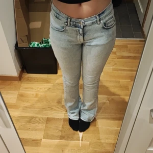 Ljusblå low flare jeans från Never Denim - Säljer ett par ljusblå jeans från Never Denim med låg midja och flare-ben. Jeansen har klassisk femficksdesign, dragkedja och knapp framtill. Perfekta för dig som gillar en retroinspirerad look med snygg passform.