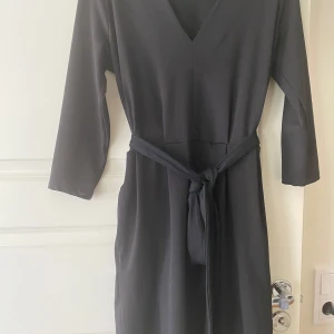 Svart omlottklänning med knytband - Säljer en svart klänning med v-ringning och knytband i midjan. Klänningen har trekvartsärm och en enkel, stilren design som passar perfekt till många tillfällen.