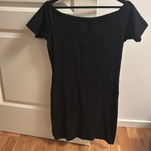 Svart kortklänning från 157 - En enkel och stilren svart kortklänning från 157 med rundad halsringning och korta ärmar. Klänningen är tillverkad i mjuk bomull med stretch för en bekväm passform. Perfekt för dig som gillar minimalistisk stil.