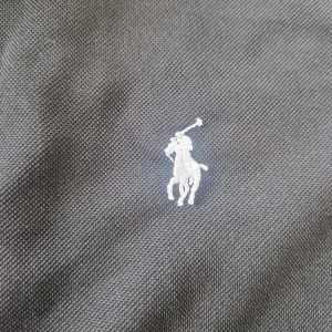 Ralph lauren thshirt - Svart t-shirt från Polo Ralph Lauren i klassisk pikéstil med korta ärmar och krage. Materialet är bomull och har en broderad vit logga på bröstet. T-shirten har knappar vid halsen och en stilren, normal passform.