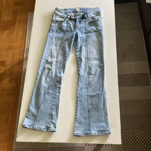 Ljusblå bootcut jeans från 157 - Snygga ljusblå jeans från 157 med bootcut passform och klassiska fem fickor. Jeansen har dubbla knappar i midjan och markerade sömmar längs benen för en cool look. Perfekta för dig som gillar retrovibbar och vill ha ett par jeans som sticker ut.
