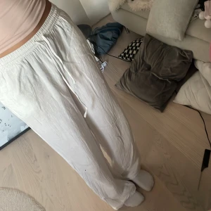 Vita linnebyxor med snörning - Säljer ett par luftiga vita linnebyxor med resår i midjan och snörning framtill. Byxorna har en relaxed fit och raka ben, perfekta för chill dagar eller när du vill ha en clean och enkel look.