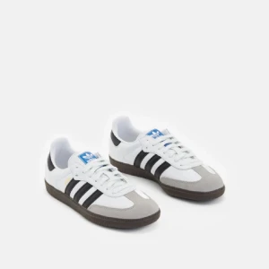 Adidas Samba sneakers - Klassiska Adidas Samba sneakers i vitt skinn med svarta ränder och grå mockadetaljer vid tån. Snygg brun sula och blå logga på plösen. Perfekta för dig som gillar retrostil och streetwear. Är använda en del men har inga defekter förutom att de är smutsiga. Jag kommer tvätta dem innan jag skickar dem!! Säljer då de blivit för små 