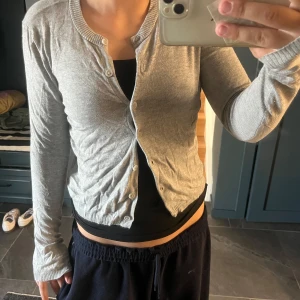 Grå kofta med knappar från lager 157 - En enkel och stilren grå kofta från lager 157 med rund halsringning och knäppning framtill. Långärmad modell i mjuk bomullsblandning, perfekt att slänga över en topp. Ribbstickade muddar vid ärmslut och nederkant för en snygg passform.