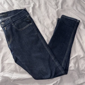 Replay Anbass mörkblå jeans, stl 28 - Snygga mörkblå Replay Anbass jeans i klassisk femficksmodell. Jeansen har raka ben, kontrastsömmar och diskret broderad bakficka. Tillverkade i stretchig denim för skön passform. Perfekta till sneakers eller boots.