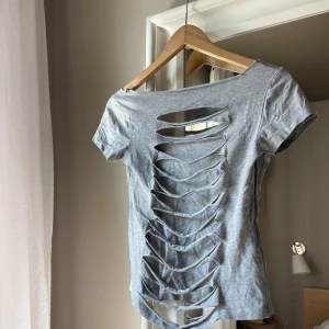 Grå t-shirt med cutout-detaljer - As cool t-shirt med snygga uppriva detaljer bak till. Tröjan är ursprungligen från lager 157 men jag har gjort om den på vissa ställen. Denna tröjan är verkligen perfekt till dig som vill ha en trendig och cool stil.💗 pris går att diskutera, skriv för fler bilder 💗