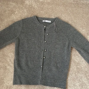Grå stickad kofta från Zara - Mysig grå stickad kofta från Zara i storlek M. Koftan har rund halsringning och pärlknappar framtill. Perfekt att slänga över en t-shirt eller klänning för en chill och stilren look.