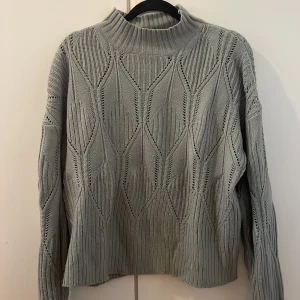 Grågrön stickad tröja med mönster från SHEIN - Snygg grågrön stickad tröja från SHEIN i storlek M. Tröjan har ett coolt grafiskt mönster, ribbad hög krage och långa ärmar. Perfekt för lager-på-lager och passar till både jeans och kjol. Materialet är mjukt i 100% akryl. 