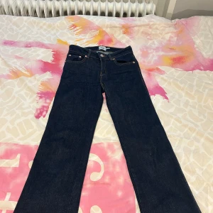 Mörkblå jeansbyxor från 157 XXS - Mörkblå jeansbyxor från 157 i storlek XXS Short. Klassisk femficksmodell 90’s bootcut och snygga bakfickor med lock och knapp. Jeansen har orange kontrastsömmar och är tillverkade i ett robust denimtyg.