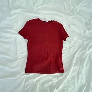 Röd t-shirt från H&M Divided - Enkel och stilren röd t-shirt från H&M Divided. Modellen är klassisk med rund halsringning och korta ärmar. Tillverkad i mjuk bomull som känns skön mot huden. Perfekt att matcha med jeans eller kjol för en clean look. Färgen är som på 3 bilden