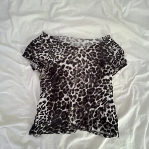 Leopardmönstrad topp  - Säljer en tunn och stretchig topp med svart och vit leopardmönster. Modellen är figurnära med korta ärmar och rund halsringning. Perfekt att styla lager på lager eller som statement-piece till jeans eller kjol.