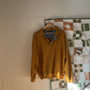 Senapsgul pikétröja från Belika - Senapsgul pikétröja från Belika med klassisk krage och half zip med tryckknappar. Tröjan har långärmad passform och ribbade muddar vid ärmslut och nederkant. Perfekt för dig som gillar retrovibbar.