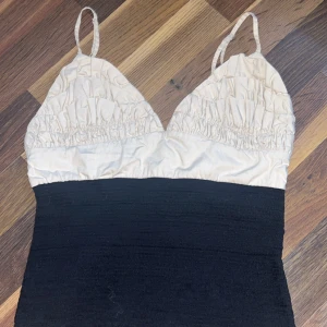 Svart och beige linne med smala axelband - Snyggt linne med smala axelband och rynkad beige överdel i kontrast mot en tight, svart underdel. Linnet har dragkedja i sidan och en figurnära passform. Perfekt för dig som gillar stilrena kontraster och enkel design.
