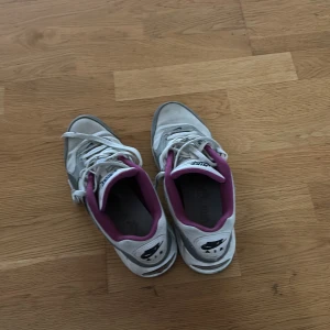 Nike Air Max sneakers vit/grå/lila - Nike Air Max sneakers i en clean mix av vitt, grått och lila. Skorna har klassisk snörning, rund tå och en mjuk plattformssula. Insidan är fodrad med lila textil för extra vibe. Perfekt för dig som gillar retrostil och streetwear.