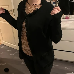 Svart kofta med fransdetaljer - Svart kofta med långa ärmar och snygga fransdetaljer längs kanterna, halsringningen och fickorna. Koftan har en enkel, rak passform och är tillverkad i ett mjukt material som känns skönt mot huden. Perfekt för dig som gillar en stilren look med lite edge. Superskön till höst/vinter❤️