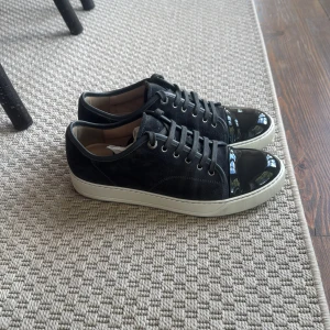 Svarta sneakers från Lanvin med lackad tå Uk6 - Snygga Gråa sneakers från Lanvin med ovandel i mocka och en glansig, lackad tå. Skorna har vita, platta sulor och klassisk snörning. Perfekt för dig som vill ha en stilren men ändå unik sneaker med exklusiv känsla. Bara skor uk6 toppen skick 10/10