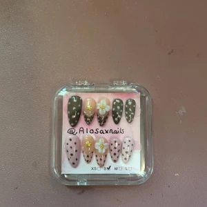 Brune og rosa prikkete kunstige negler - Fine kunstige negler i mandelform med en miks av brune og lyserosa nyanser, dekorert med prikker, 3D-blomster og små gullstjerner. Settet inneholder 10 negler i ulike størrelser, perfekte for å skape en unik og søt look. Håndlaget og levert i en praktisk eske.