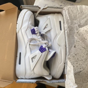 Nike Air Jordan 4 Retro 'Court Purple' - Nike Air Jordan 4 Retro i vitt skinn med lila metallic detaljer och klassisk Jumpman-logga på plös och häl. Snygg meshpanel på sidorna, snörning och chunky sula. Perfekta för dig som vill sticka ut med en clean och modern sneaker. Skorna är använda 2 gånger dem är väldigt bekväma och fräscha. Slutades använda då jag bytte stil. Pris kan diskuteras.