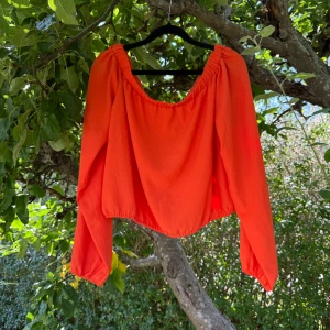 Orange croppad blus med resår - Superfin orange croppad blus från Bikbok med långa ärmar och resår i både halsringning och nederkant. Snygg offshoulder-look och luftig passform som ger en cool vibe till din outfit. Perfekt för dig som vill sticka ut med färg och stil. Storlek L. Helt ny med tags/ prislapp fortfarande kvar. 