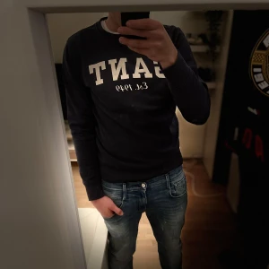 Mörkblå sweatshirt från GANT - Säljer en mörkblå sweatshirt från GANT med vit logga och texten 'Est. 1949' på bröstet. Tröjan har rund halsringning och långa ärmar. Perfekt för dig som gillar klassisk och stilren streetwear.