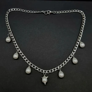 Silverhalsband med droppformade pärlor - Kedjehalsband i silverfärgad metall med sju hängande droppformade vita pärlor, varav en har en unik spikdetalj. Kedjan är chunky och ger ett coolt statement. Perfekt för dig som gillar edgy men ändå stilrena accessoarer.