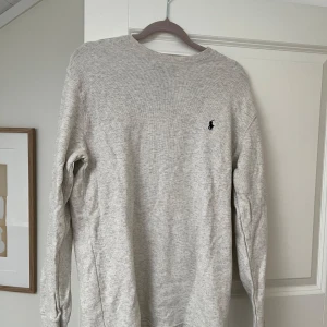  Långärmad tröja från Polo Ralph Lauren - Säljer en stilren ljusgrå/beige långärmad tröja från Polo Ralph Lauren med diskret broderad logga på bröstet. Tröjan är i mjuk bomull och har en klassisk passform med rund hals. Perfekt för en clean och avslappnad look. Använd fåtal gånger. Nypris 1499. 