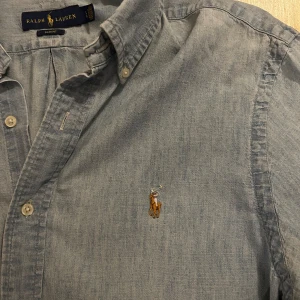 Blå skjorta från Ralph Lauren - Snygg Jeans skjorta från Ralph Lauren i slim fit-modell. Skjortan har klassisk krage, långa ärmar och knäppning framtill. Perfekt för en ren look 