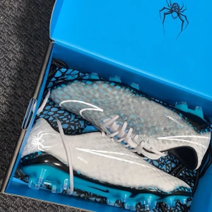 Nike hypervenom hydra rgn(Helt nya) - Nike Hypervenom fotbollsskor i grått med blå och svarta detaljer, coolt mönstrad ovandel och sula. Skorna har snörning, rund tå och platt sula med dobbar för gräsplan. Snyggt Hypervenom-tryck och spindelgrafik på hälen. Perfekt för dig som vill sticka ut på planen.