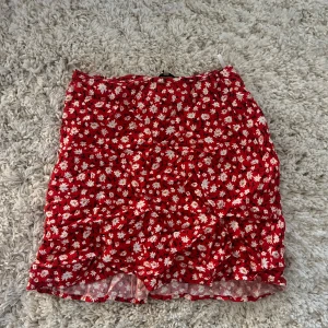 Röd blommig kortkjol i S - Superfin röd kortkjol med blommigt mönster i vitt och gult. 