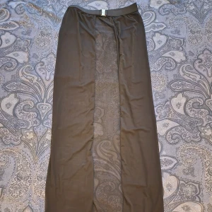 Svart strandkjol i mesh - Svart pullover/strandkjol i mesh med snyggt guldspänne framtill. Kjolen är transparent och sensuell. Bältet ger extra edge och markerar midjan på ett stilrent sätt.