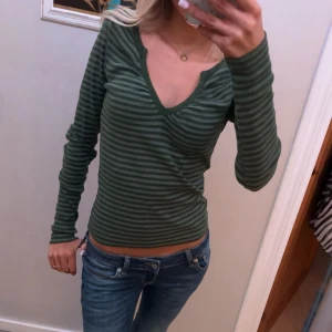 Grön randig långärmad tröja - Snygg grön långärmad tröja med smala mörkgröna och ljusgröna ränder. Tröjan har en djup v-ringning och sitter tight mot kroppen. Perfekt att styla med jeans för en chill och trendig look. Köpt secondhand och saknar lappar, skulle gissa på att de e en storlek S☺️