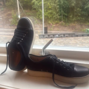 Lanvins - Snygga svarta sneakers från Lanvin med ovandel i skinn och mocka, vita gummisulor och klassisk snörning. Skorna har rund tå och diskreta metalldetaljer vid snörhålen. Perfekta för dig som gillar stilrena och exklusiva sneakers med lyxig känsla. OBS!! KAN GÅ NER PÅ PRIS VID SNABB AFFÄR🤝🍀
