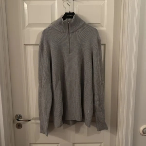 Grå ribbad stickad tröja half zip - Snygg grå stickad tröja med ribbad struktur och half zip-dragkedja i halsen. Perfekt för lager-på-lager och har en hög krage som ger extra stilpoäng. Långärmad och passar dig som gillar en clean och enkel look.