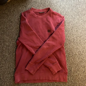 Vinröd sweatshirt från J.Lindeberg - Vinröd sweatshirt från J.Lindeberg med rund hals och svart logga på bröstet. Tröjan har långa ärmar och ribbade muddar vid ärmslut och nederkant. Perfekt för dig som gillar stilren och enkel design. Bra skick, använd en del, stl m och passar dig runt 180. Bara att höra av sig vid frågor eller liknande!