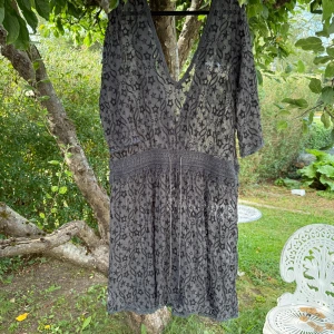 Grå spetsklänning Odd Molly stjärnmönster - Supersöt grå kortklänning från Odd Molly med broderade svarta stjärnor och transparent spets. Djup v-ringning, trekvartsärm och knyt i midjan. Perfekt för dig som gillar unika detaljer och boho-vibe. Storlek 1 som enligt deras storleksguide motsvarar en storlek S. Men den är rymlig i storlek. Kanske mer en M.  Mycket fint skick, jag hittar inga synliga anmärkningar eller defekter. 