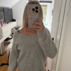 Grå offshoulder stickad tröja - Supermysig grå stickad tröja med bred ribbad kant runt halsen som sitter snyggt offshoulder. Perfekt för dig som gillar chill och stilren vibe. Långärmad och loose fit, passar till jeans eller kjol. Materialet är mjukt och värmande, perfekt för kyliga dagar.