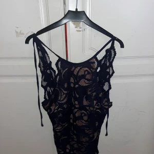 Mörkblå spetsig korsett-topp - Säljer en snygg mörkblå korsett-topp med spetsdetaljer och tunna axelband. Toppen har ett genombrutet spetsmönster och nude-färgad insida som ger en cool kontrast. Perfekt för dig som vill sticka ut med en trendig och feminin look.