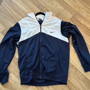 Nike vindjacka i marinblå och vit - Nike tunn vindjacka i storlek L. Jackan har hel dragkedja, höga muddar och två sidofickor.