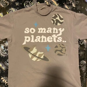 Broken planet T-shirt - Säljer en tjock broken planet t-shirt med coolt planetsprint och texten 'so many planets..' på framsidan och 'how do i find mine?' på baksidan. T-shirten har korta ärmar, kort rund hals och tryck i beige, vitt och blått. Materialet känns som mjuk bomull, perfekt för chill dagar.