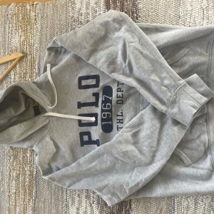 Grå hoodie från Polo Ralph Lauren - Säljer en grå hoodie från Polo Ralph Lauren. Det står L på den men den passar mer M/S eftersom den råka krympa i tvätten så fortfarande i väldigt bra skick