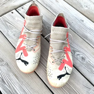 Puma fotbollsskor med röd detalj - Säljer ett par grymma fotbollsskor från Puma med beige stickad strumpkrage och snörning. Skorna har en cool röd zigzag-detalj på sidorna och svarta Puma-loggor framtill. Ovandelen är syntet med prickigt mönster och platt sula med dobbar för gräsplan.