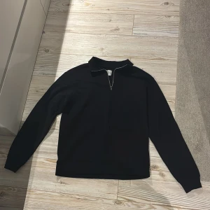 Svart half zip tröja Jack & Jones - Svart långärmad tröja från Jack & Jones med krage och half zip-dragkedja framtill. Enkel och clean design utan mönster, perfekt för chill dagar. Materialet känns mjukt och är troligtvis bomull eller polyester. Snygg passform som funkar till vad som helst. Helt oanvänd. 